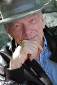 Portrait of High Mountain Sheriff series author Edward Massey wearing felt cowboy hat, leather jacket and blue shirt