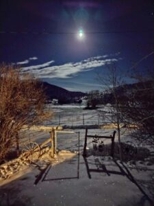 Dawn light touches a wooden wheel and gate at the snow-dusted valley of Pineview Farm